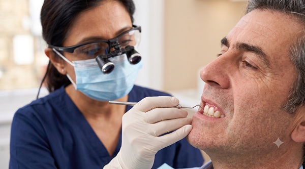 A clinical exterior close-up of a dentist examining a single dental implant crown. The gum tissue immediately surrounding the crown shows subtle redness and early swelling (peri-implantitis), distinct from healthy tissue, without explicit interior view. The head and facial proportions are anatomically correct and natural.