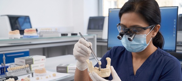 A detailed, photorealistic clinical view inside a professional dental laboratory in Istanbul. A female technician using magnification loupes carefully verifies the micro-precision of a single, standard human-sized Straumann implant abutment. A full standard human mandible replica in the foreground confirms the components are realistic human scale, small, and not oversized, demonstrating the technical rigor of warranty remediation.